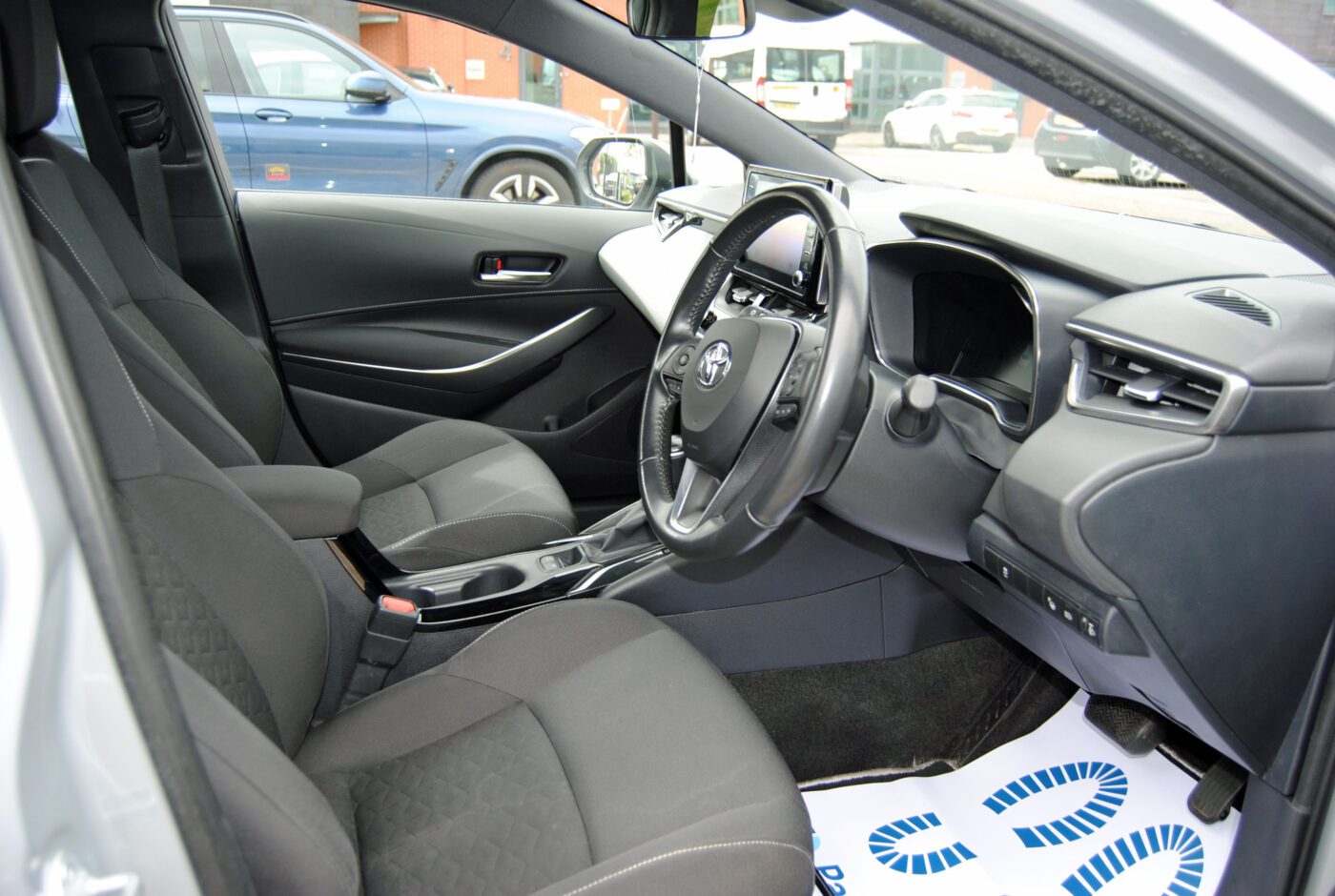 Front interior of a Toyota Corolla . Two seats and the steering wheel in view.