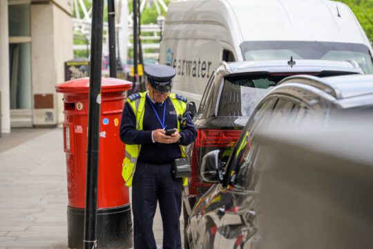 Traffic warden stood next to a red post-box whist writing up a parking ticket