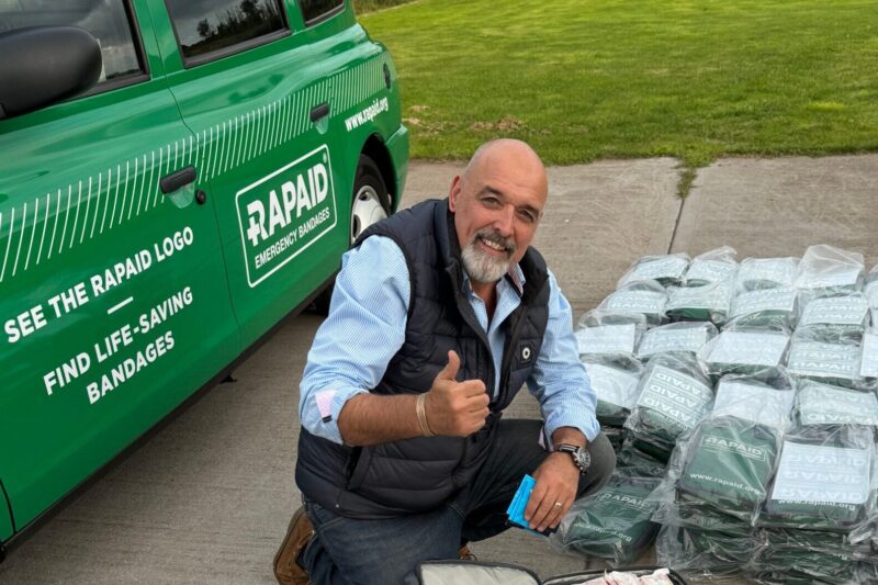 Rapaid emergency bleed kits laid in front of a branded Rapaid taxi cab. Smiling man packing the kits into a box.