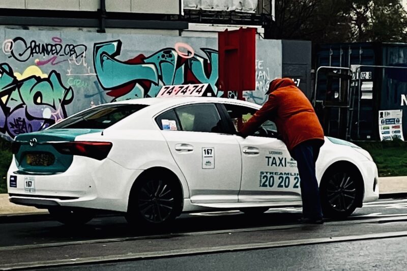 White taxi with operator liveries on the door, speaking to a passenger through window.