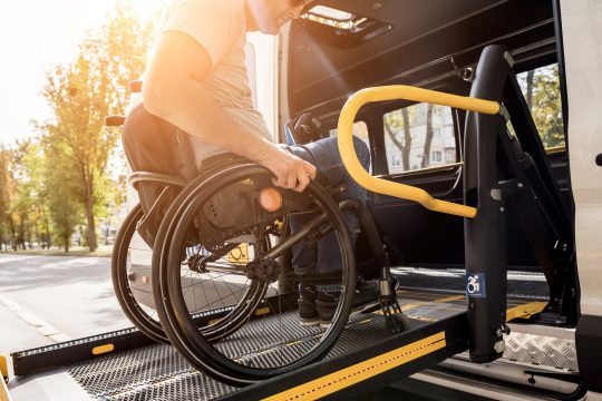 A man in a wheelchair getting into an accessible taxi using a vehicle ramp