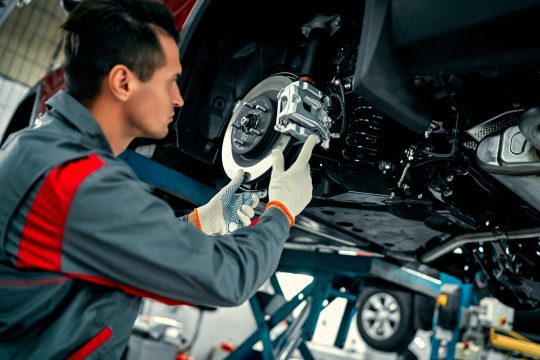 Car mechanic worker repairing suspension of lifted automobile at auto repair garage shop station